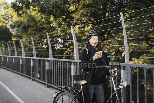 Jeune femme debout à vélo et utilisant le téléphone — Photo de stock