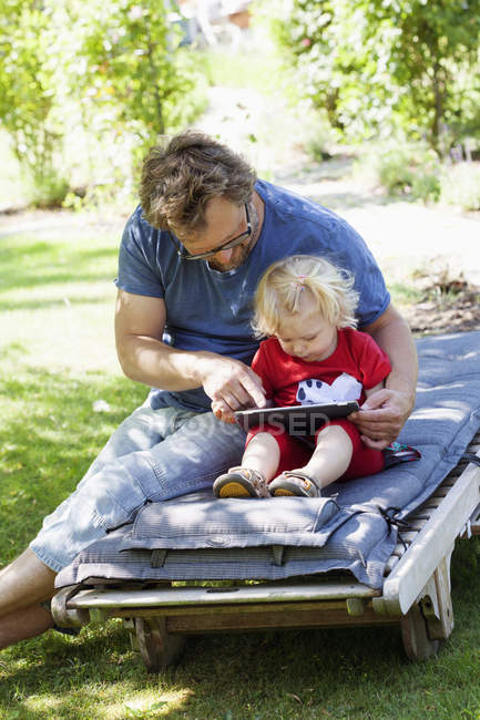 Daughter with father sitting on deckchair and using tablet pc — Stock Photo