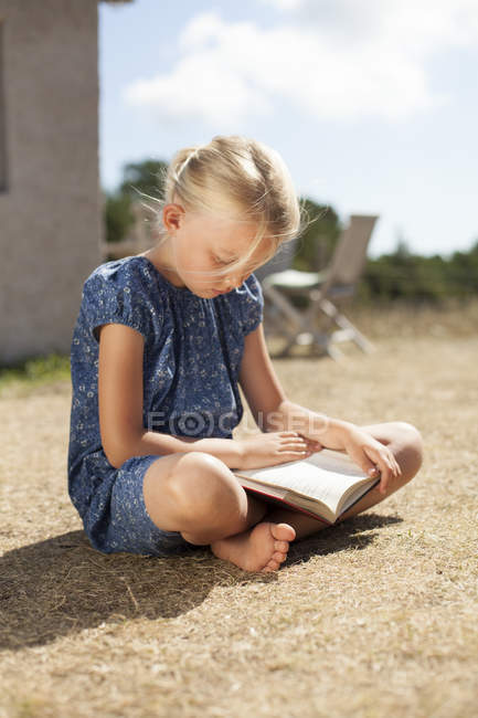 Девушка читает книгу сидя на заднем дворе, избирательный фокус — стоковое фото