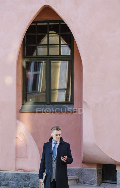 Businessman standing by building arch and using smart phone — Stock Photo