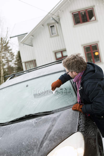 Man scraping ice off car windshield at winter — Stock Photo