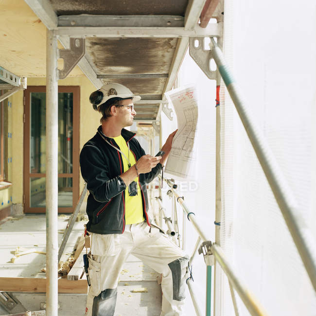 Bauarbeiter schaut sich Baupläne an und nutzt Smartphone — Stockfoto