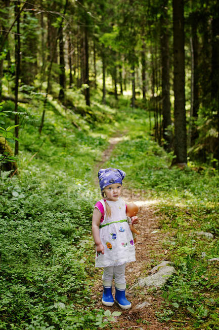 Retrato de menina com boneca olhando para câmera na floresta — Fotografia de Stock