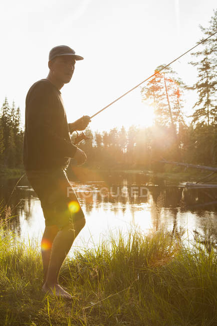 Man in baseball cap with fishing rod in sunlight — Stock Photo