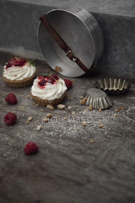 Fresh Baked raspberry cakes decorated with cream and raspberries on table with baking forms — Stock Photo