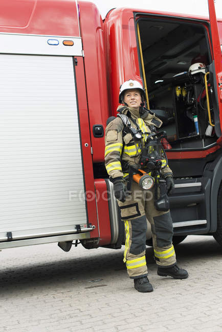 Female firefighter in uniform standing by fire engine — Stock Photo