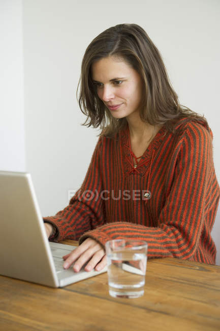 Jeune femme utilisant un ordinateur portable à la table — Photo de stock