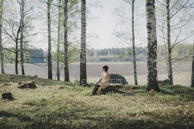 Jovem mulher sentada no toco na floresta — Fotografia de Stock
