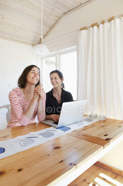 Женщины смеются и используют ноутбук в гостиной — стоковое фото
