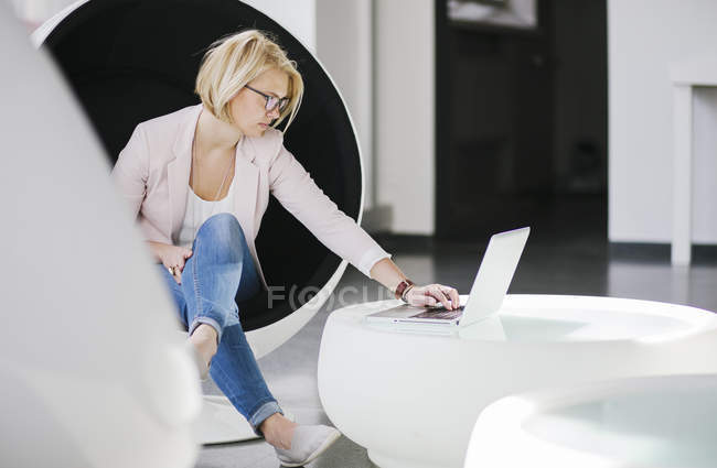 Woman using laptop in ball chair, differential focus — Stock Photo