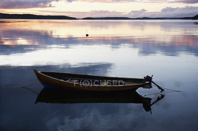 Човен причалив на морській воді з відображенням хмарного заходу сонця неба — стокове фото