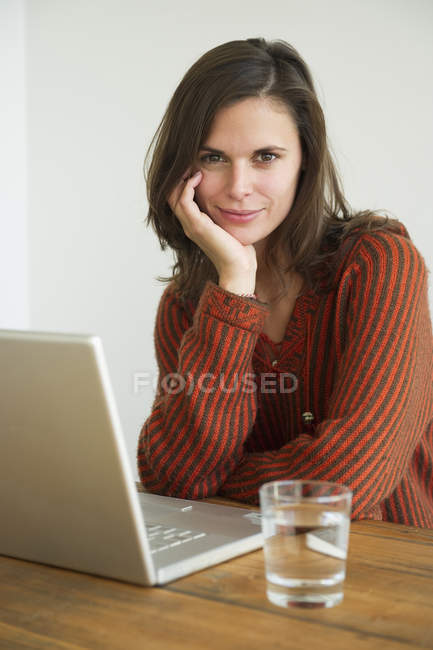Vue de la jeune femme assise avec un ordinateur portable et regardant la caméra — Photo de stock