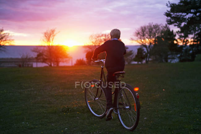 Rückansicht eines Jungen, der bei Sonnenuntergang radelt — Stockfoto