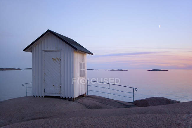 Casa de praia em rochas por mar na luz do pôr-do-sol — Fotografia de Stock