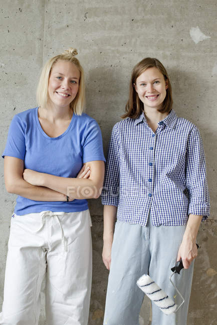 Mujeres jóvenes de pie junto a la pared y sosteniendo rodillo de pintura - foto de stock