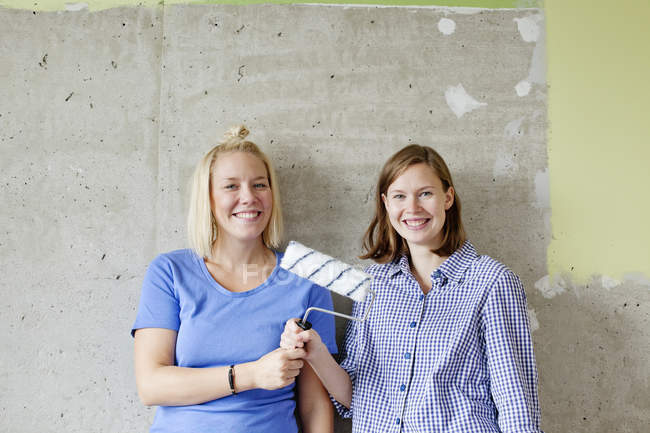Mujeres jóvenes de pie junto a la pared y sosteniendo rodillo de pintura - foto de stock