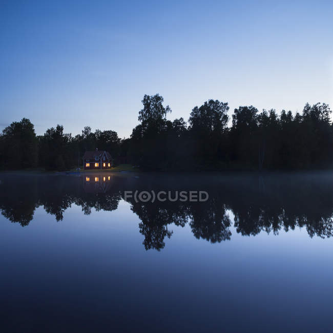 Pequena cabana com janelas iluminadas no lago à noite — Fotografia de Stock