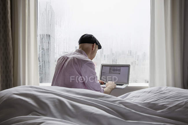 Чоловік сидить на ліжку і використовує ноутбук — стокове фото