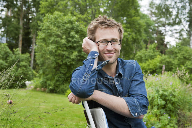 Portrait of man sitting on chair in backyard — Stock Photo