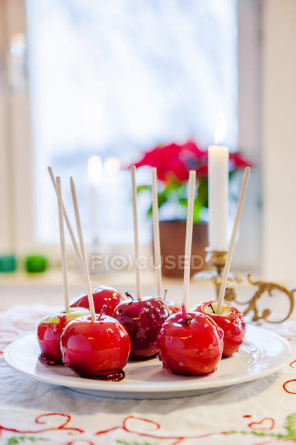 Teller mit kandierten Äpfeln mit Stöcken auf Küchentheke neben Fenster — Stockfoto
