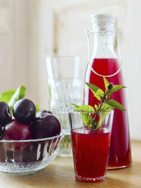 Carafe and glass with plum juice and bowl of whole plums — Stock Photo
