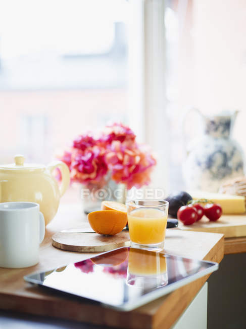 Mesa de desayuno con zumo de naranja fresca y tableta digital - foto de stock