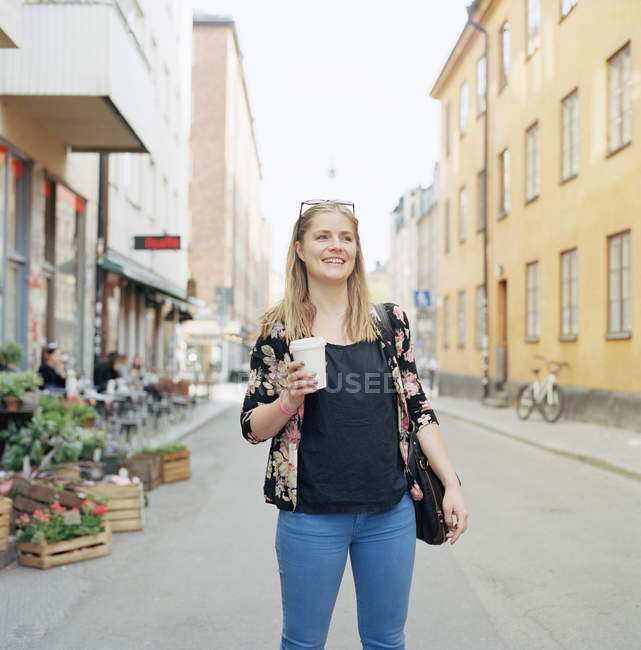 Mulher loira sorridente com xícara de café na rua da cidade — Fotografia de Stock
