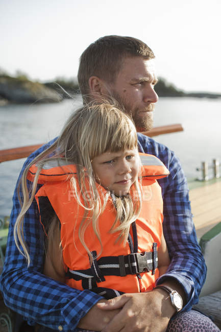 Girl in life jacket sitting on father laps — Stock Photo