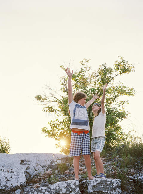 Dos chicos parados en la roca con las manos arriba - foto de stock