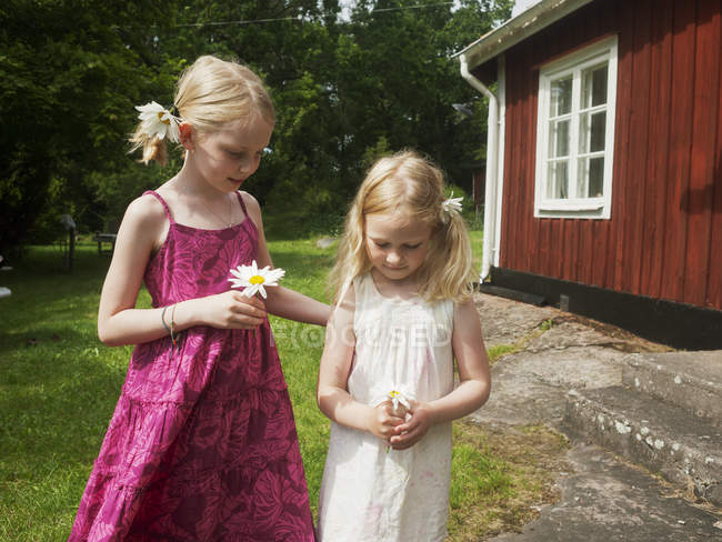 Dos chicas sosteniendo flores de marguerite en frente de la casa - foto de stock