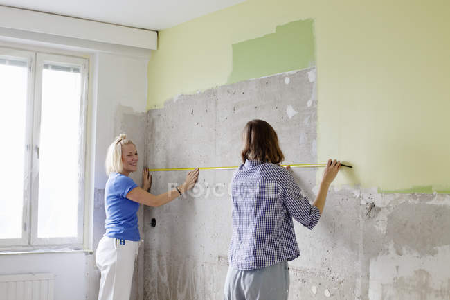 Mujeres jóvenes midiendo la pared para la renovación - foto de stock