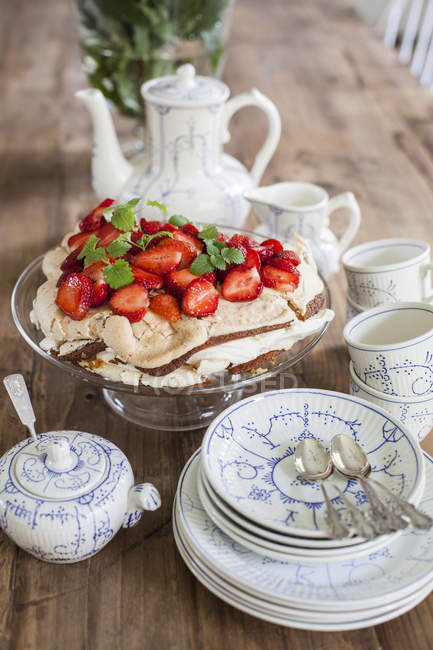 Tisch mit Tassen und Untertassen und Erdbeer-Wüste auf Kuchen — Stockfoto