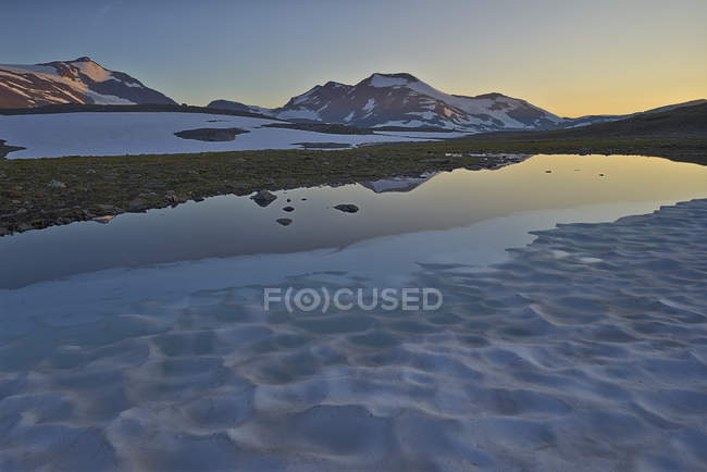 Snocapped mountains and lake water at sunset — Stock Photo