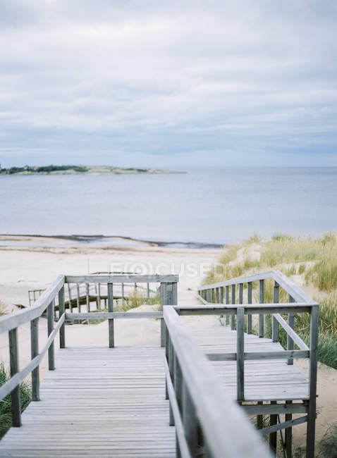 Wooden steps leading to sandy beach with cloudy sky — Stock Photo