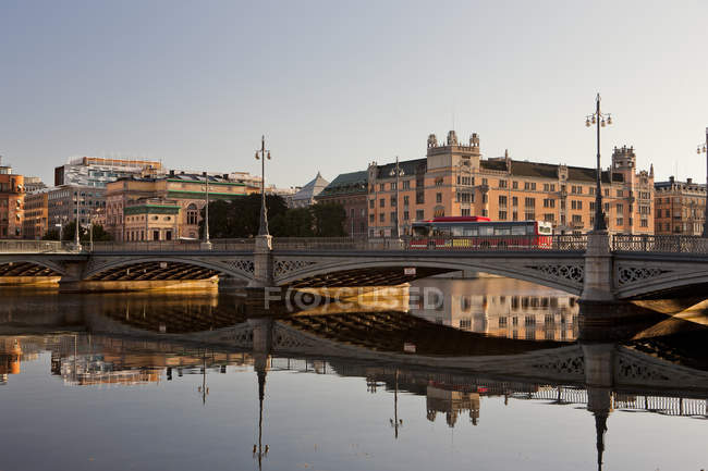 Bridge with riding bus and buildings reflecting in harbor water — Stock Photo