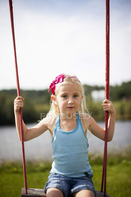 Girl with blonde hair sitting on rope swing — Stock Photo