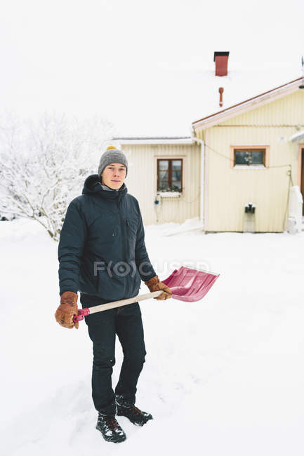 Homme debout avec une pelle à neige rose devant la maison — Photo de stock