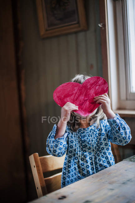Girl holding paper heart in front of face — Stock Photo