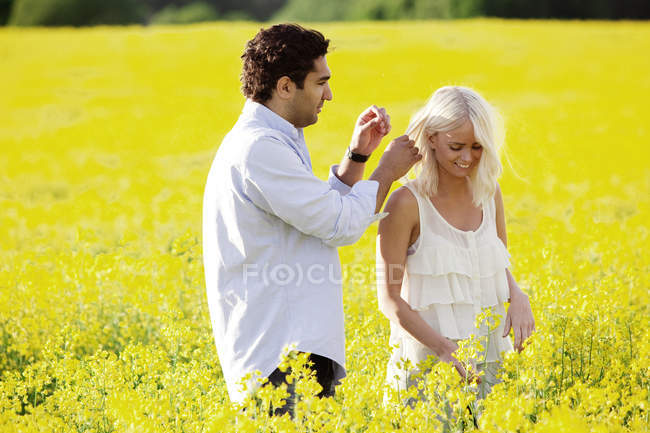 Улыбающаяся молодая пара, обнимающая поле, фокусирующаяся на переднем плане — стоковое фото