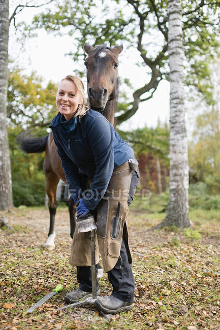 Sorrindo mulher de pé por cavalo no arvoredo — Fotografia de Stock
