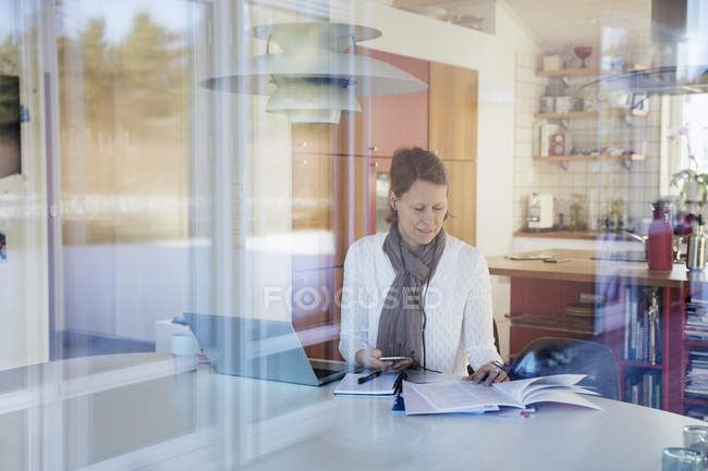 Reife Frau liest Dokumente und benutzt Laptop — Stockfoto
