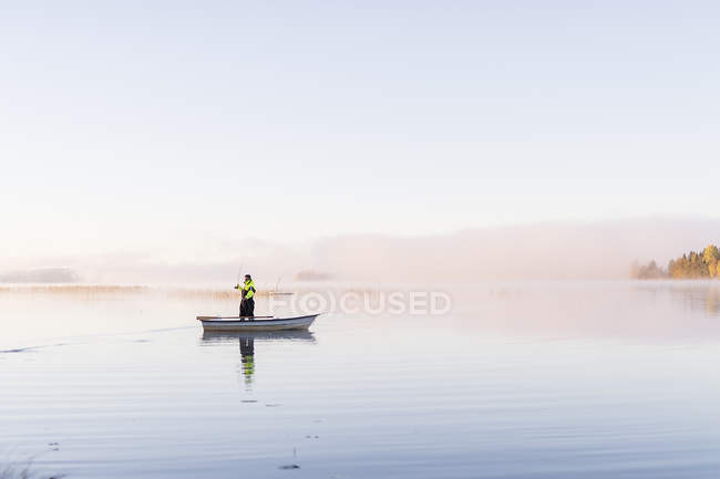 Jeune homme pêche dans le lac au coucher du soleil — Photo de stock