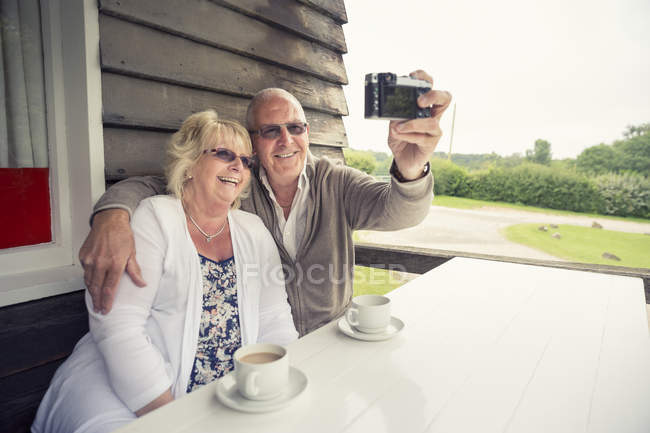 Seniorenpaar sitzt am Tisch auf Veranda und macht Selfie mit Kamera — Stockfoto
