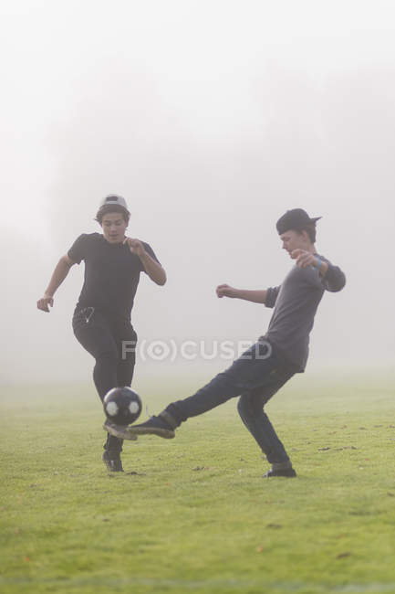 Teenage boys playing soccer at foggy lawn — Stock Photo