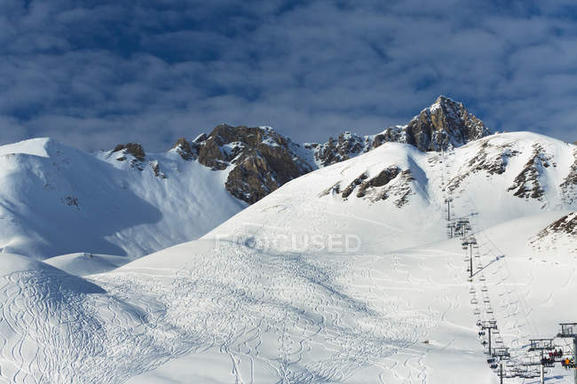 Vista del telesilla en las montañas nevadas bajo el cielo azul nublado - foto de stock