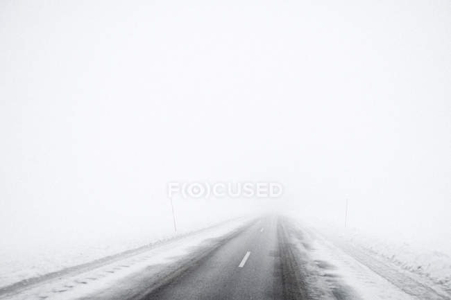 Дорога згасає в тумані в критому снігу ландшафті — стокове фото