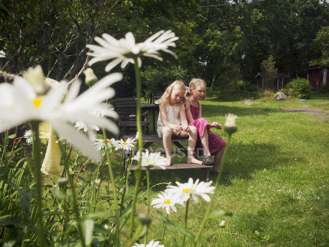 Two girls sitting on wooden bench in domestic garden — Stock Photo