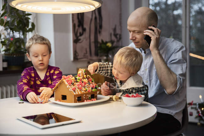 Man and two boys decorating gingerbread house — Stock Photo