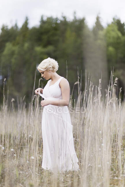 Mulher de vestido branco em pé no prado entre plantas secas — Fotografia de Stock