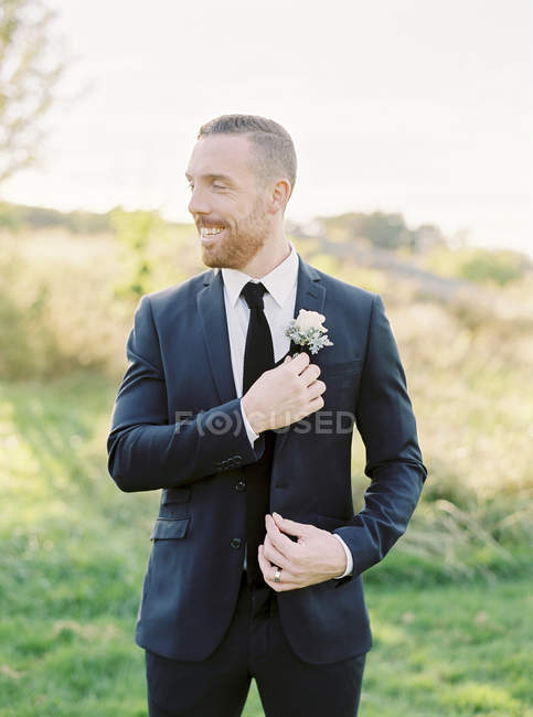 Portrait of groom standing and adjusting boutonniere — Stock Photo